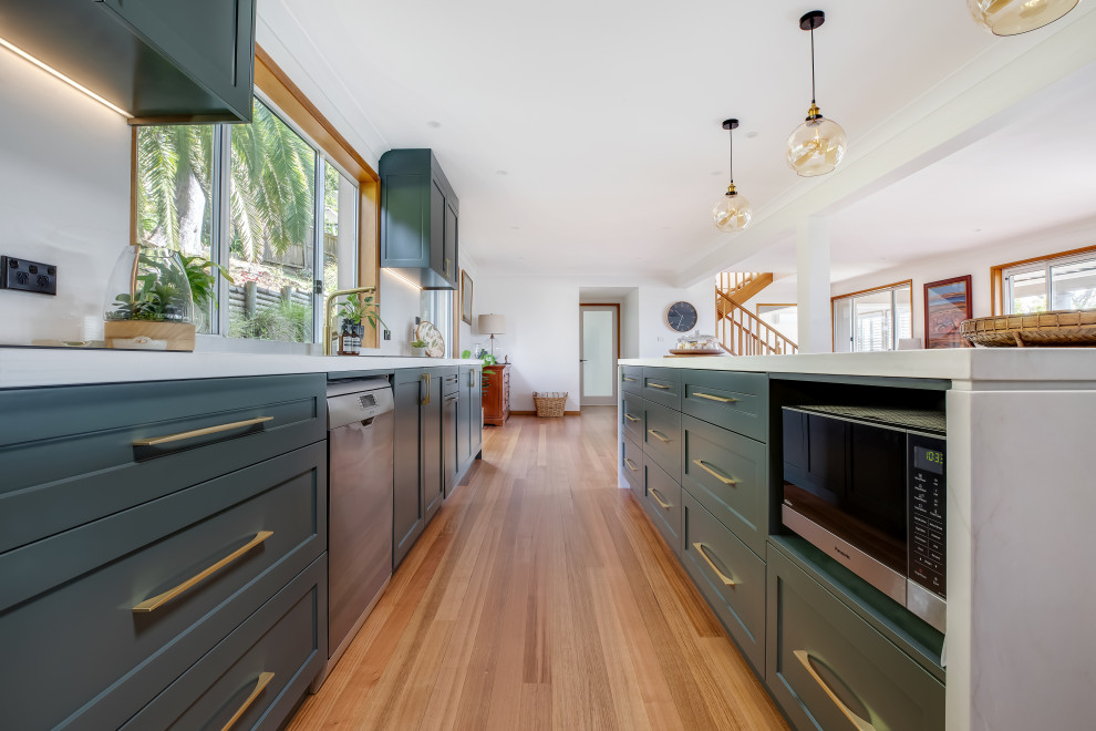 Eat-in kitchen - large transitional l-shaped medium tone wood floor and multicolored floor eat-in kitchen idea in Sydney with a drop-in sink, shaker cabinets, green cabinets, quartz countertops, white backsplash, quartz backsplash, black appliances, an island and white countertops
