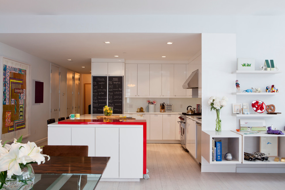 This is an example of a mid-sized scandinavian l-shaped open plan kitchen in New York with an undermount sink, flat-panel cabinets, white cabinets, solid surface benchtops, white splashback, glass sheet splashback, stainless steel appliances, light hardwood floors, with island and red benchtop.