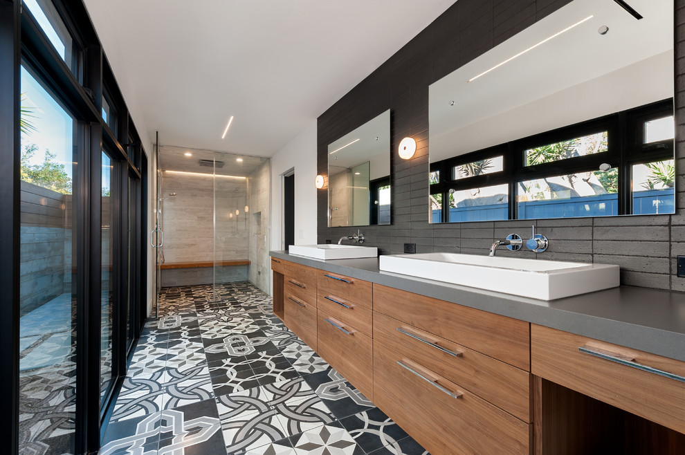 Photo of a large contemporary master bathroom in San Diego with a trough sink, flat-panel cabinets, medium wood cabinets, an alcove shower, black tile, white walls, engineered quartz benchtops, a wall-mount toilet, cement tile, concrete floors, multi-coloured floor and a hinged shower door.