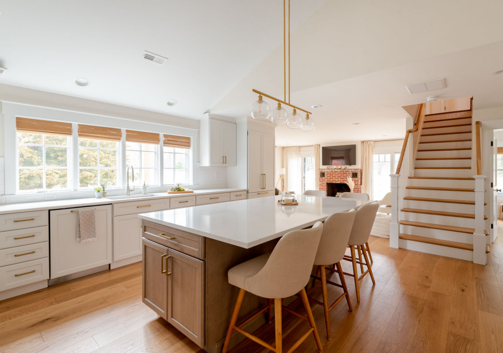 Example of a huge transitional l-shaped light wood floor, brown floor and vaulted ceiling eat-in kitchen design in Boston with an undermount sink, shaker cabinets, white cabinets, quartz countertops, white backsplash, ceramic backsplash, paneled appliances, an island and white countertops