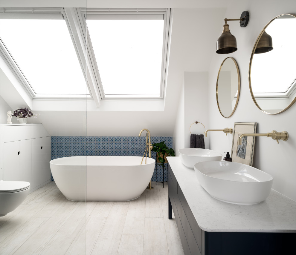Design ideas for a contemporary ensuite bathroom in London with flat-panel cabinets, black cabinets, a freestanding bath, a built-in shower, a wall mounted toilet, mosaic tiles, white walls, wood-effect flooring, a vessel sink, marble worktops, beige floors, an open shower, white worktops, double sinks, a built in vanity unit and a vaulted ceiling.