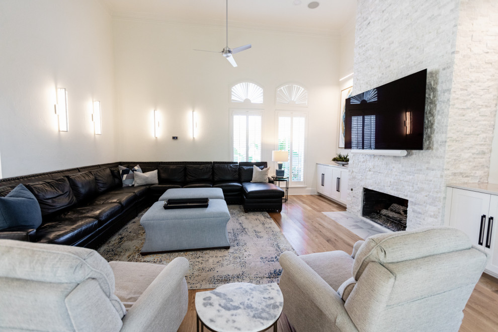 Imagen de sala de estar abierta minimalista grande con paredes blancas, suelo de madera clara, todas las chimeneas, piedra de revestimiento, televisor colgado en la pared y suelo marrón