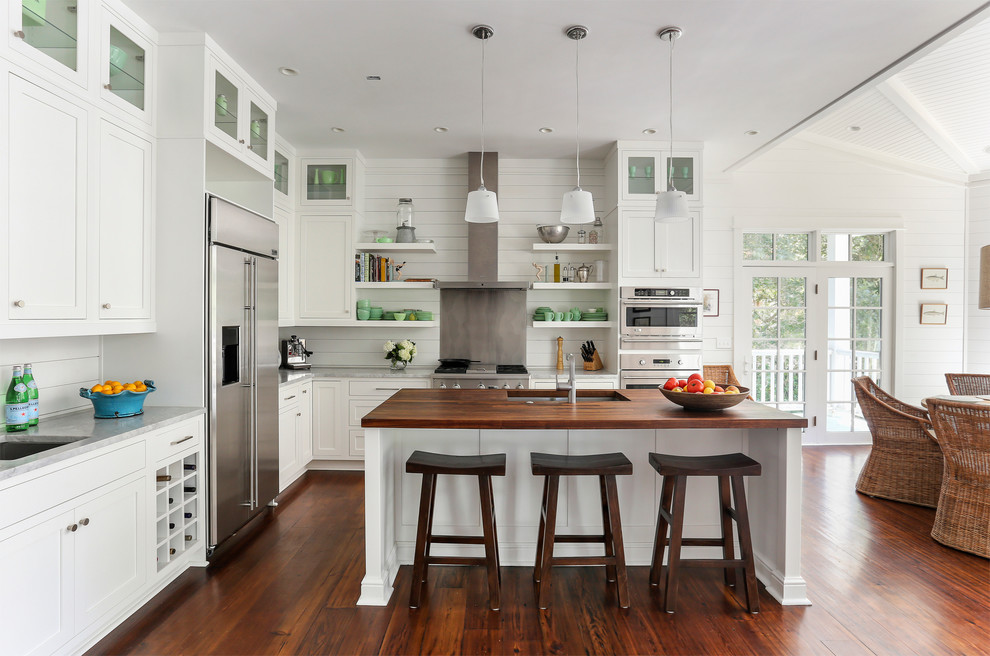 Photo of a beach style l-shaped open plan kitchen in Charleston with an undermount sink, recessed-panel cabinets, white cabinets, wood benchtops, white splashback and stainless steel appliances.