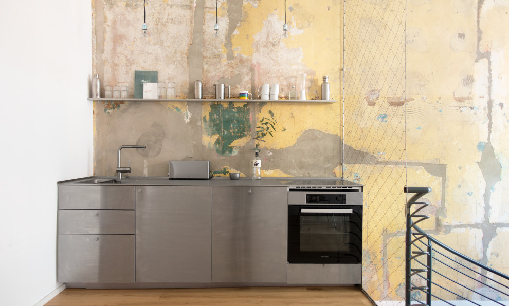 This is an example of a mid-sized contemporary single-wall eat-in kitchen in Berlin with an integrated sink, flat-panel cabinets, stainless steel cabinets, stainless steel benchtops, multi-coloured splashback, stainless steel appliances, light hardwood floors, no island, beige floor and grey benchtop.