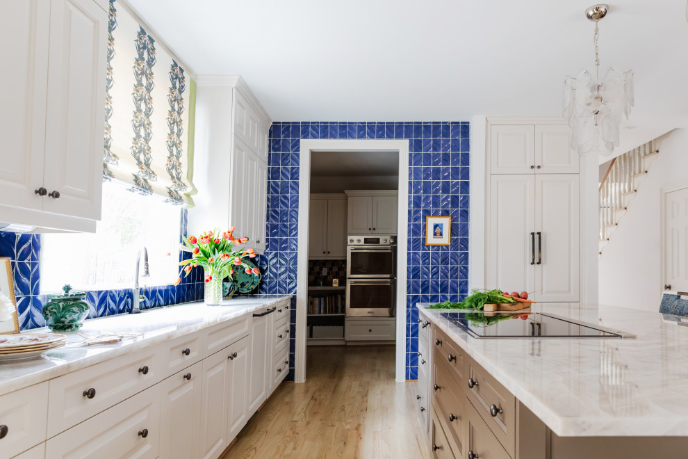 Klassisk inredning av ett mellanstort vit vitt kök, med en köksö, granitbänkskiva, blått stänkskydd, stänkskydd i keramik, rostfria vitvaror, ljust trägolv, brunt golv, en undermonterad diskho, luckor med upphöjd panel och vita skåp