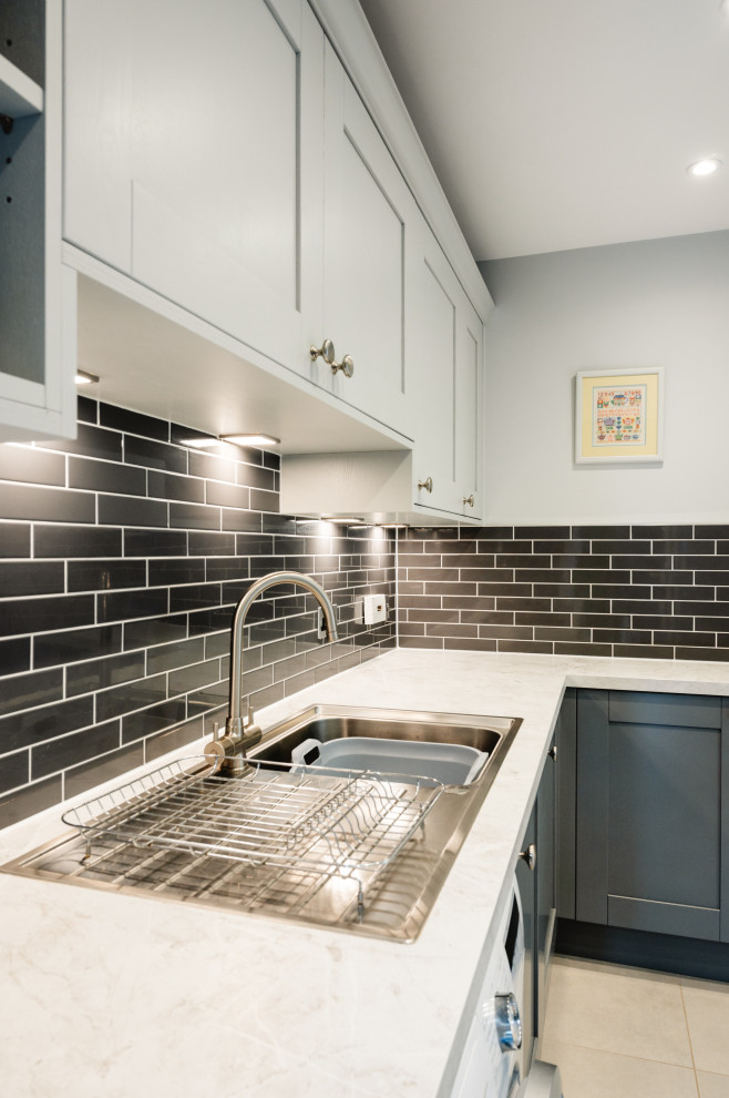 Photo of a mid-sized traditional l-shaped utility room in Surrey with a single-bowl sink, shaker cabinets, grey cabinets, laminate benchtops, grey splashback, ceramic splashback, grey walls, porcelain floors, grey floor and white benchtop.