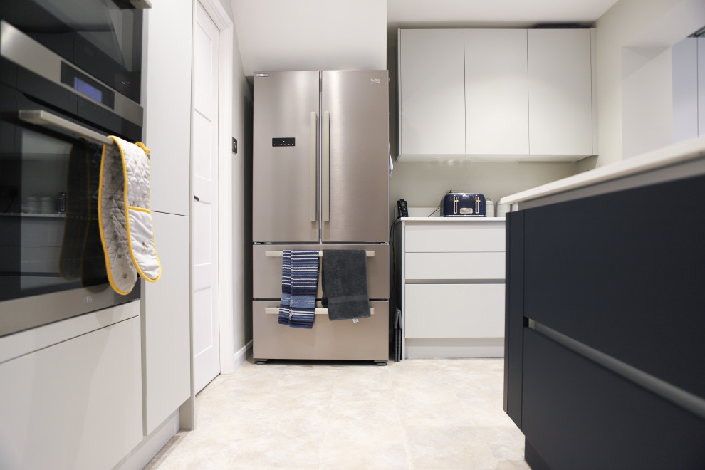 Medium sized contemporary cream and black open plan kitchen in Essex with an integrated sink, flat-panel cabinets, black cabinets, stainless steel appliances, an island, multi-coloured floors and white worktops.