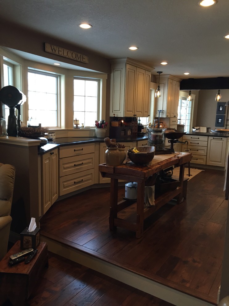 Enclosed kitchen - mid-sized rustic l-shaped dark wood floor enclosed kitchen idea in Minneapolis with a farmhouse sink, raised-panel cabinets, distressed cabinets, granite countertops, black backsplash, stainless steel appliances and an island