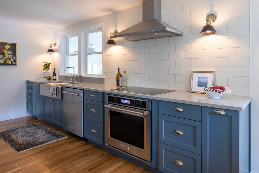 Bild på ett vintage grå grått kök, med skåp i shakerstil, blå skåp, bänkskiva i kvarts, vitt stänkskydd, stänkskydd i keramik, rostfria vitvaror och mellanmörkt trägolv