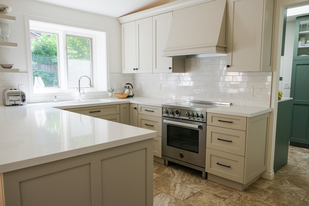 Example of a mid-sized transitional u-shaped ceramic tile, beige floor and vaulted ceiling eat-in kitchen design in Vancouver with an undermount sink, shaker cabinets, beige cabinets, quartz countertops, white backsplash, porcelain backsplash, stainless steel appliances, a peninsula and white countertops