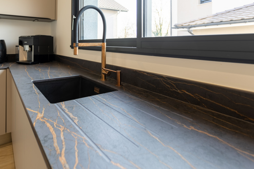 Idéer för att renovera ett mellanstort funkis svart svart kök, med en integrerad diskho, luckor med profilerade fronter, beige skåp, kaklad bänkskiva, svart stänkskydd, stänkskydd i keramik, integrerade vitvaror, ljust trägolv, en köksö och brunt golv