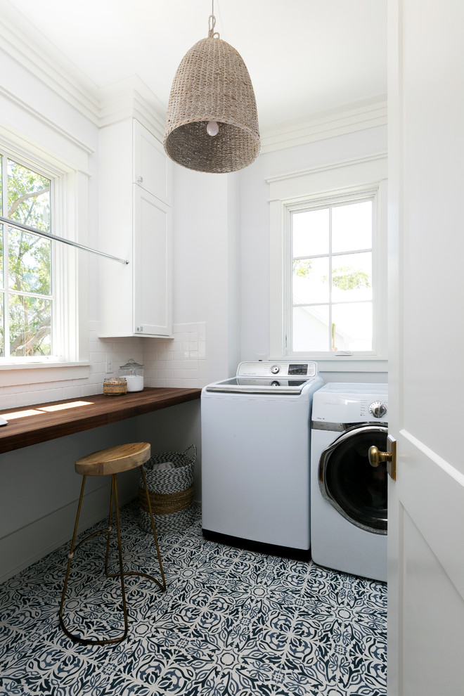 Photo of a mid-sized country l-shaped dedicated laundry room in Charleston with recessed-panel cabinets, white cabinets, wood benchtops, white walls, ceramic floors, a side-by-side washer and dryer, multi-coloured floor and brown benchtop.