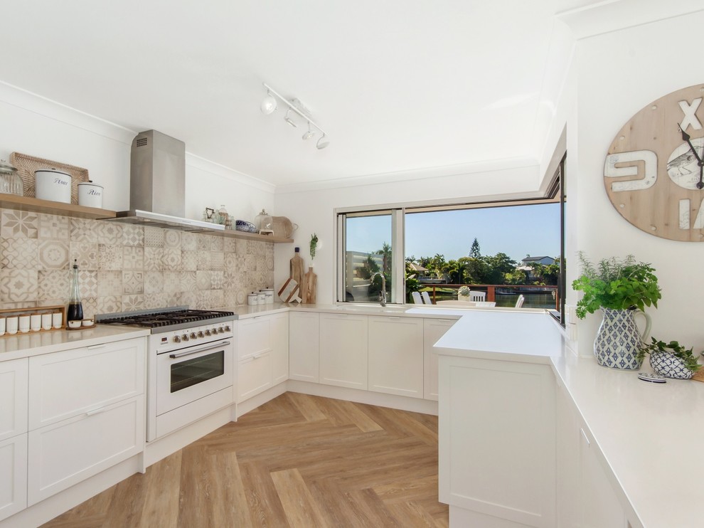 Design ideas for a large beach style u-shaped kitchen in Gold Coast - Tweed with an undermount sink, shaker cabinets, white cabinets, quartz benchtops, ceramic splashback, white appliances and vinyl floors.