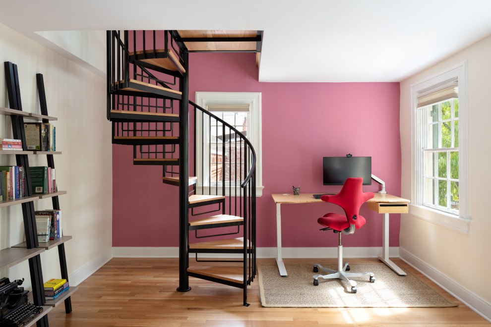Стильный дизайн: рабочее место с розовыми стенами, паркетным полом среднего тона, отдельно стоящим рабочим столом и коричневым полом - последний тренд