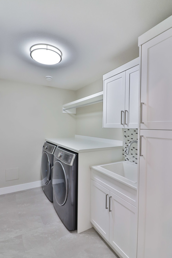 This is an example of a large transitional galley dedicated laundry room in Other with an utility sink, shaker cabinets, white cabinets, laminate benchtops, grey walls, vinyl floors, a side-by-side washer and dryer and grey floor.