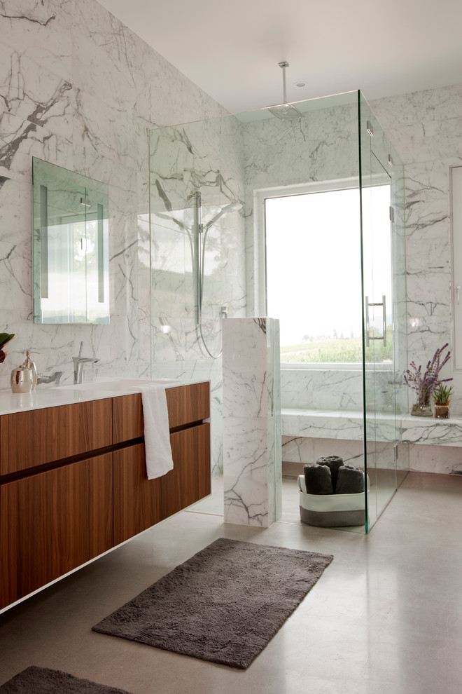 Design ideas for a large contemporary master bathroom in Vancouver with flat-panel cabinets, dark wood cabinets, a curbless shower, white tile, gray tile, a drop-in tub, stone slab, white walls, concrete floors, an integrated sink, solid surface benchtops, white benchtops and a shower seat.