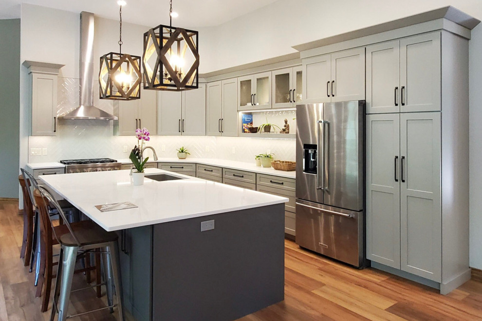 Inspiration for an arts and crafts l-shaped eat-in kitchen in Grand Rapids with a farmhouse sink, shaker cabinets, grey cabinets, quartzite benchtops, blue splashback, glass sheet splashback, stainless steel appliances, vinyl floors, with island, brown floor and white benchtop.