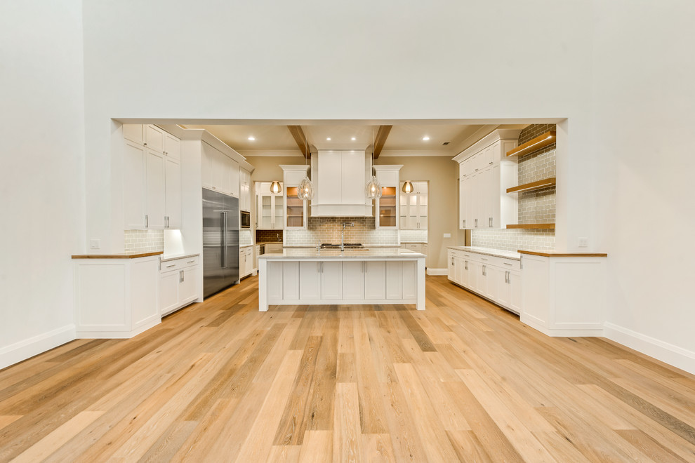 This is an example of a large contemporary u-shaped eat-in kitchen in Dallas with an undermount sink, flat-panel cabinets, white cabinets, quartzite benchtops, brown splashback, glass tile splashback, stainless steel appliances, light hardwood floors and with island.