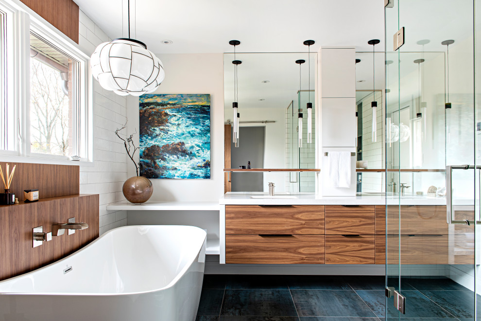 Photo of a large contemporary ensuite bathroom in Toronto with flat-panel cabinets, medium wood cabinets, a freestanding bath, white tiles, white walls, porcelain flooring, a submerged sink, engineered stone worktops, turquoise floors, white worktops, double sinks and a floating vanity unit.