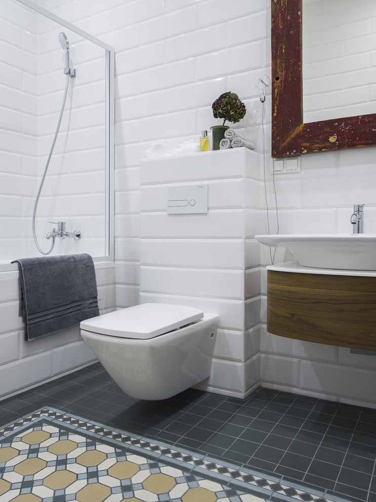 This is an example of a contemporary ensuite bathroom in Moscow with flat-panel cabinets, medium wood cabinets, an alcove bath, a shower/bath combination, a wall mounted toilet, white tiles, metro tiles, a vessel sink and multi-coloured floors.