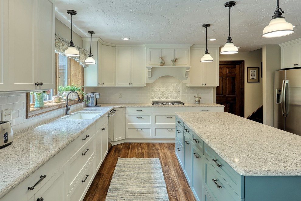 Transitional vinyl floor and brown floor kitchen photo with an undermount sink, white cabinets, quartz countertops, white backsplash, subway tile backsplash, stainless steel appliances, an island and beige countertops