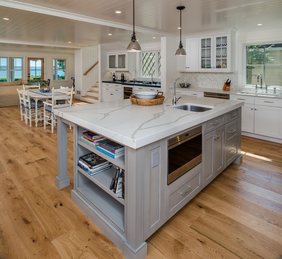 Large beach style open plan kitchen in Other with an undermount sink, shaker cabinets, white cabinets, quartz benchtops, white splashback, stainless steel appliances, light hardwood floors, with island, beige floor, white benchtop and marble splashback.