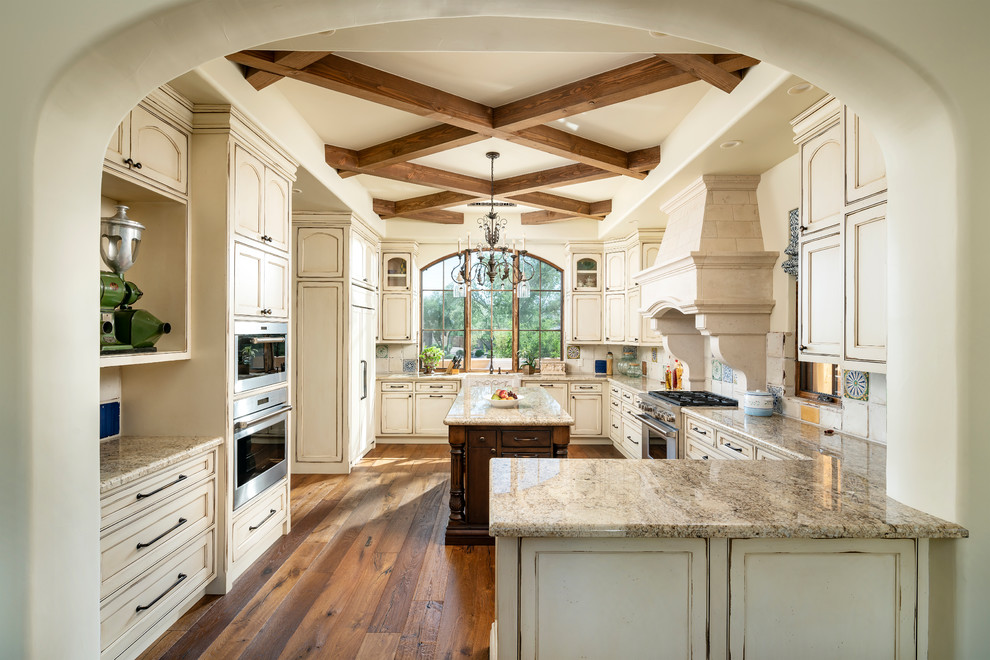 Traditional u-shaped kitchen in Phoenix with a farmhouse sink, recessed-panel cabinets, distressed cabinets, beige splashback, stainless steel appliances, medium hardwood floors, brown floor and beige benchtop.
