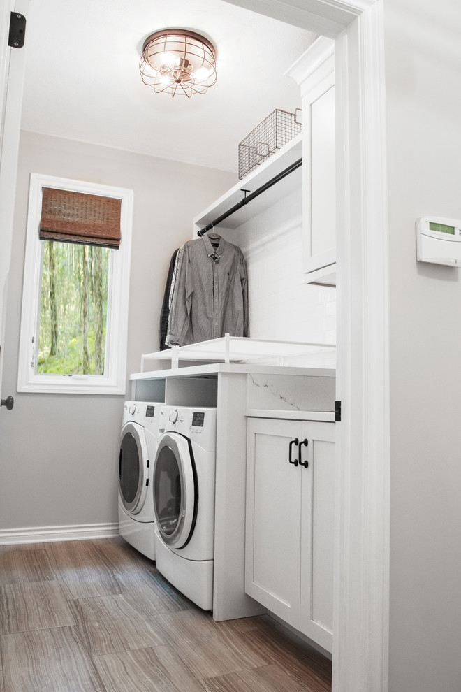 This is an example of a mid-sized transitional single-wall dedicated laundry room in Grand Rapids with a single-bowl sink, shaker cabinets, white cabinets, quartz benchtops, grey walls, porcelain floors and a side-by-side washer and dryer.