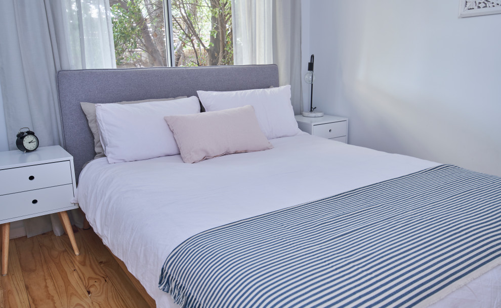 Cette image montre une petite chambre minimaliste avec un mur blanc, un sol en bois brun et un sol beige.