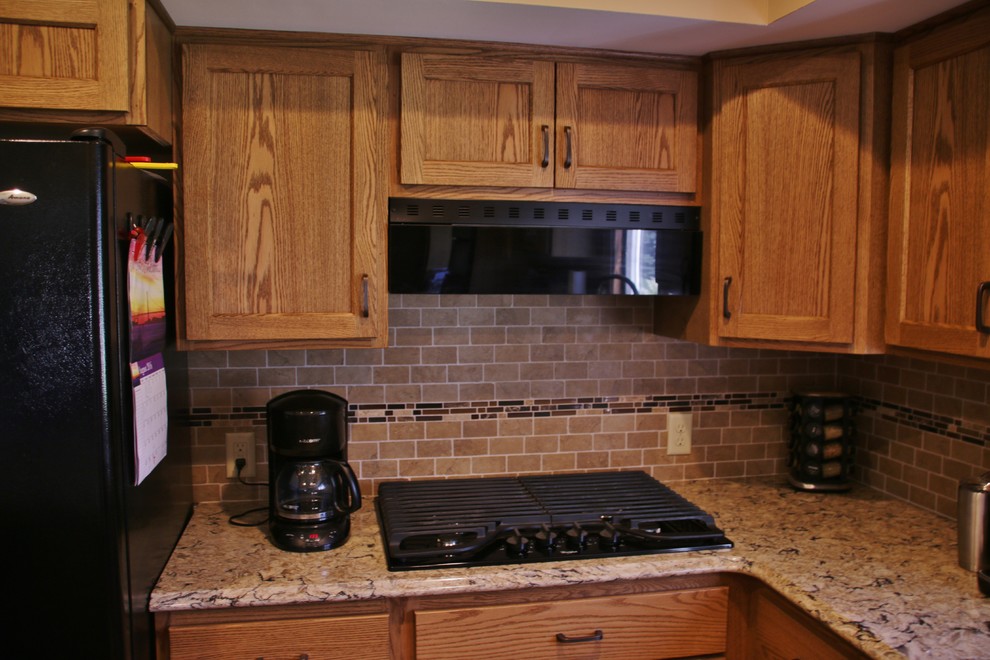 Example of a mid-sized l-shaped eat-in kitchen design with flat-panel cabinets, medium tone wood cabinets, quartz countertops, beige backsplash, black appliances and an island