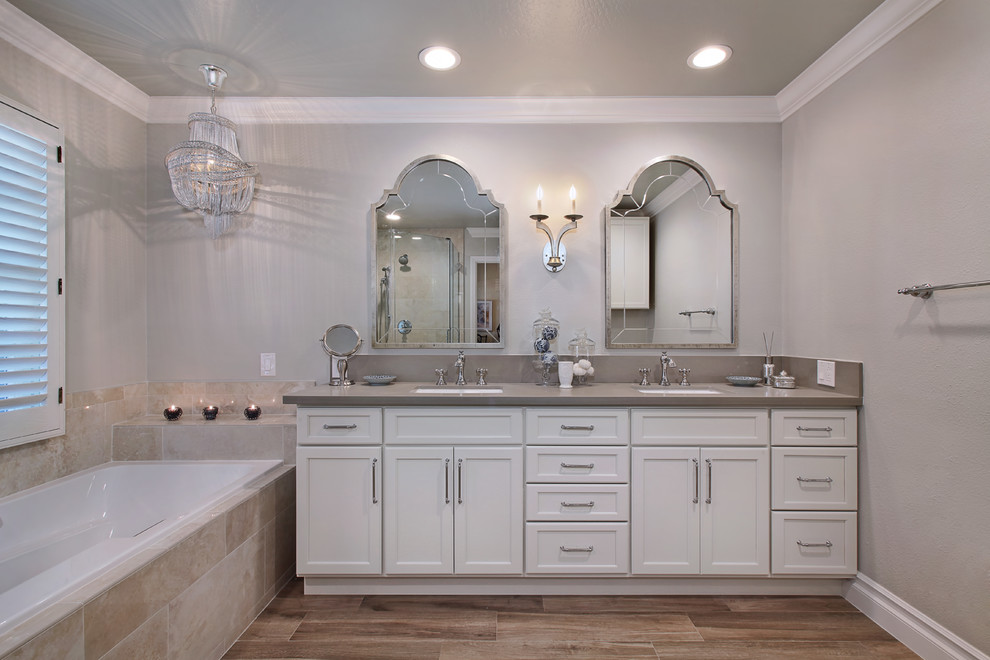 This is an example of a mid-sized transitional master bathroom in Orange County with shaker cabinets, white cabinets, a drop-in tub, a corner shower, a one-piece toilet, beige tile, stone tile, grey walls, porcelain floors, an undermount sink and engineered quartz benchtops.