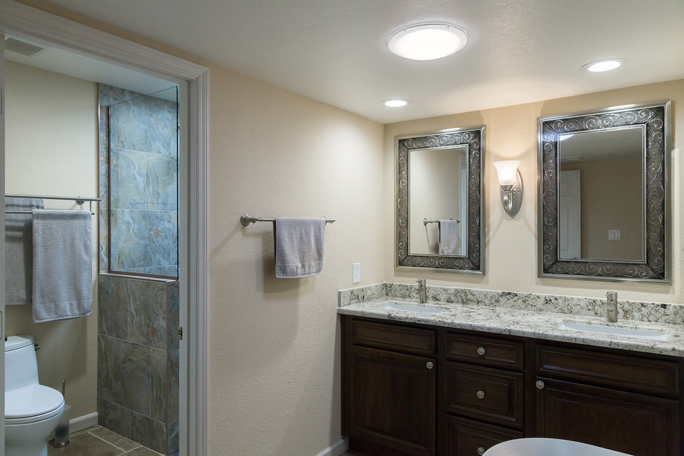 Example of a mid-sized transitional master gray tile and porcelain tile porcelain tile and brown floor walk-in shower design in Phoenix with shaker cabinets, dark wood cabinets, a one-piece toilet, beige walls, an undermount sink, granite countertops and beige countertops