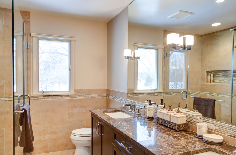 This is an example of a transitional bathroom in Chicago with an undermount sink, flat-panel cabinets, dark wood cabinets, marble benchtops, a corner shower, a two-piece toilet, beige tile and porcelain tile.