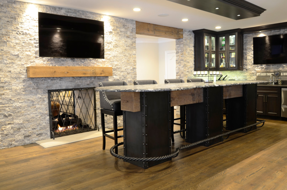 Inspiration for an expansive transitional seated home bar in Milwaukee with an undermount sink, recessed-panel cabinets, dark wood cabinets, granite benchtops, grey splashback, stone tile splashback, medium hardwood floors, brown floor and grey benchtop.