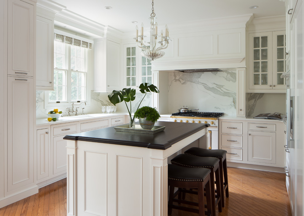 Inspiration for a transitional u-shaped kitchen in New York with a single-bowl sink, glass-front cabinets, white splashback, marble splashback, medium hardwood floors, with island and white appliances.