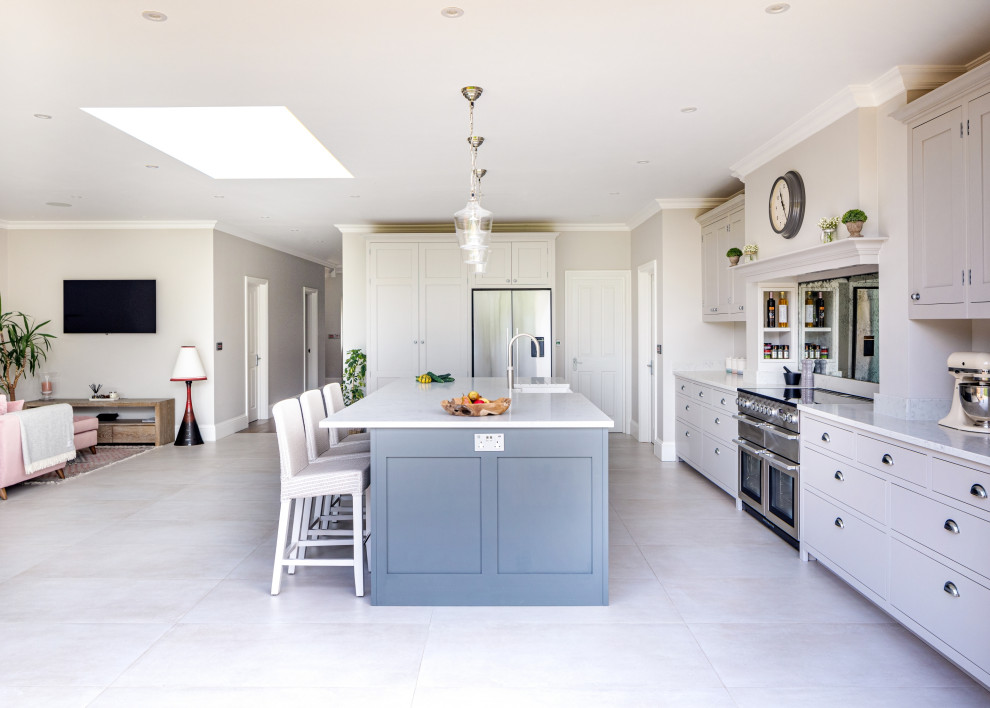 Photo of a mid-sized traditional l-shaped eat-in kitchen in Surrey with a farmhouse sink, shaker cabinets, grey cabinets, quartzite benchtops, grey splashback, mirror splashback, stainless steel appliances, porcelain floors, with island, grey floor and white benchtop.