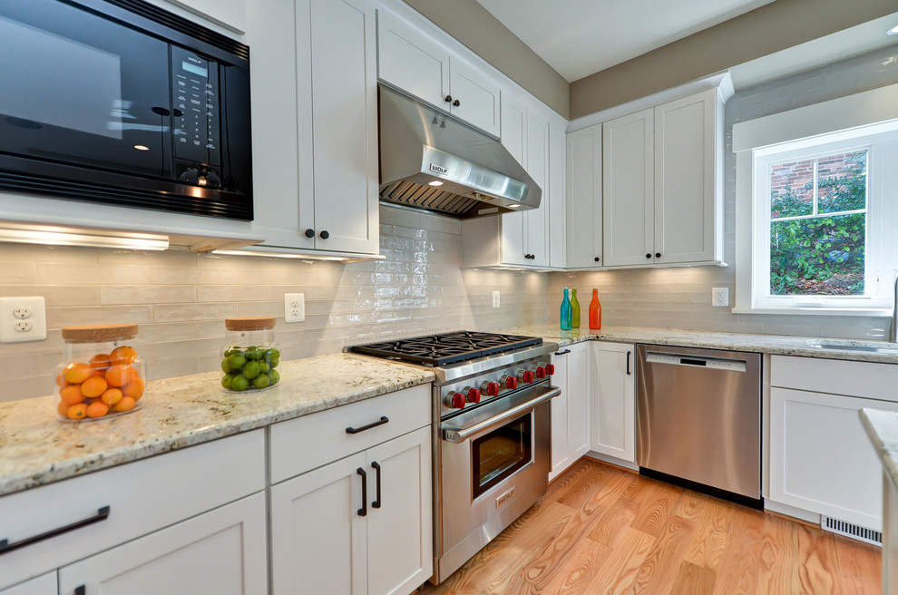 Design ideas for a transitional l-shaped kitchen in DC Metro with shaker cabinets, white cabinets, grey splashback, stainless steel appliances, light hardwood floors and with island.
