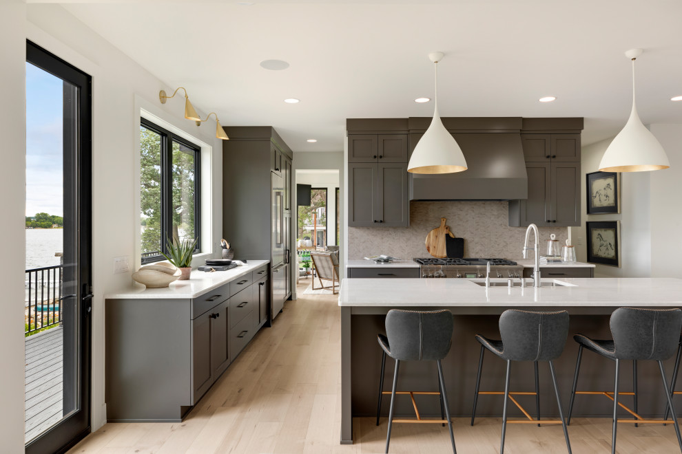 Transitional kitchen in Minneapolis with a drop-in sink, quartz benchtops, stainless steel appliances, light hardwood floors, with island and white benchtop.