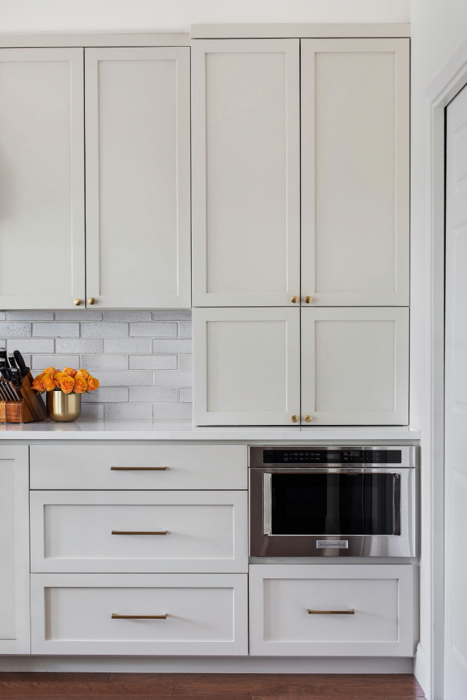 Inspiration for a mid-sized transitional medium tone wood floor and brown floor open concept kitchen remodel in Austin with an undermount sink, shaker cabinets, gray cabinets, quartz countertops, white backsplash, brick backsplash, stainless steel appliances, a peninsula and white countertops