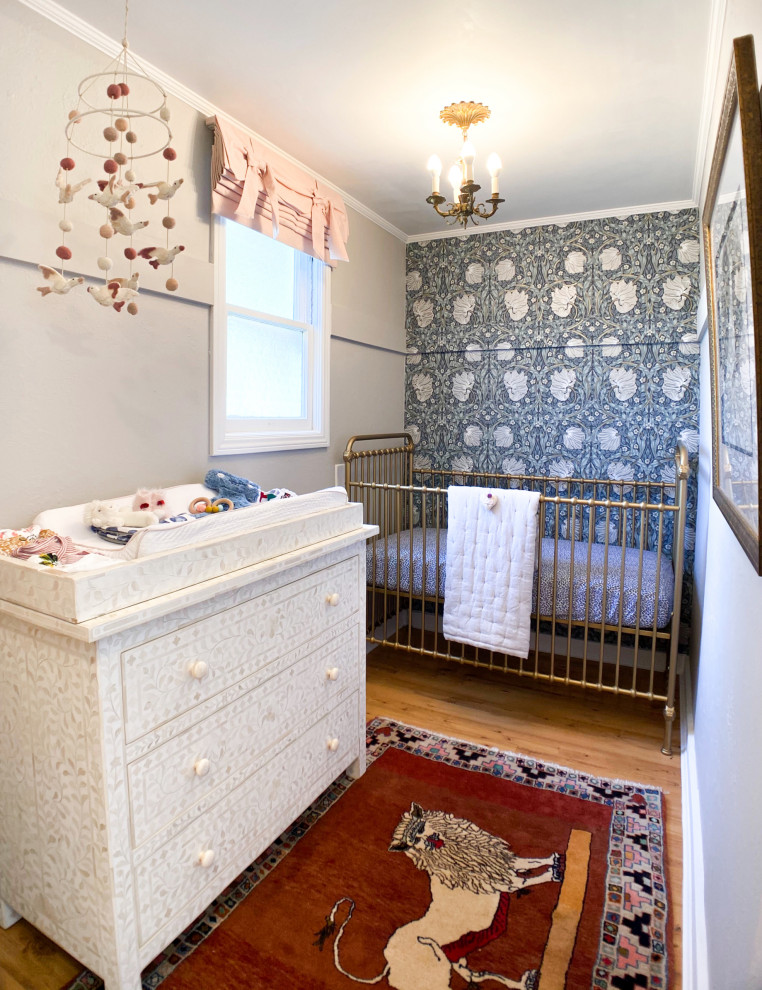 Cette photo montre une petite chambre de bébé neutre éclectique avec un mur blanc, un sol en bois brun et du papier peint.