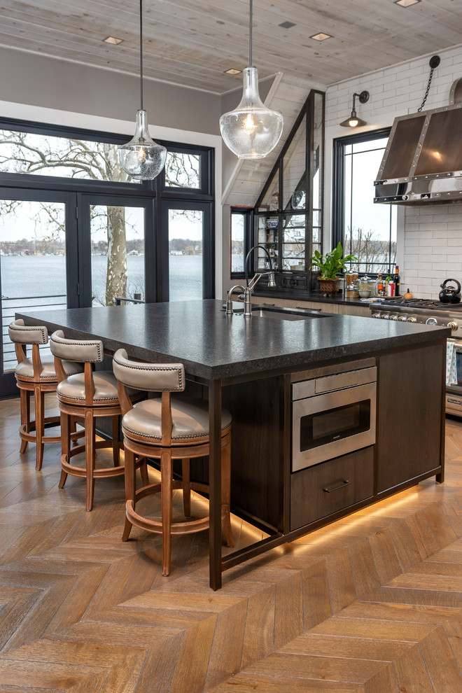 Photo of a mid-sized industrial l-shaped separate kitchen in Other with a double-bowl sink, flat-panel cabinets, brown cabinets, granite benchtops, white splashback, stainless steel appliances, medium hardwood floors, with island, beige floor, black benchtop and cement tile splashback.