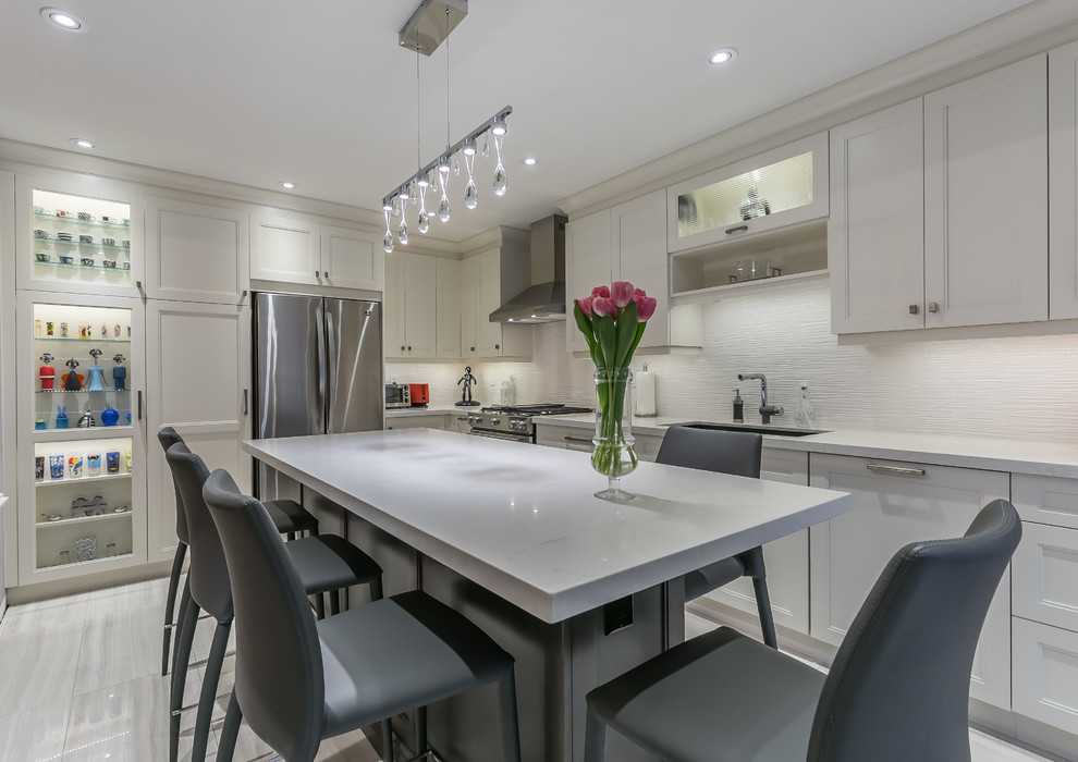 Inspiration for a mid-sized transitional l-shaped porcelain tile eat-in kitchen remodel in Toronto with a drop-in sink, recessed-panel cabinets, white cabinets, quartz countertops, stainless steel appliances and an island