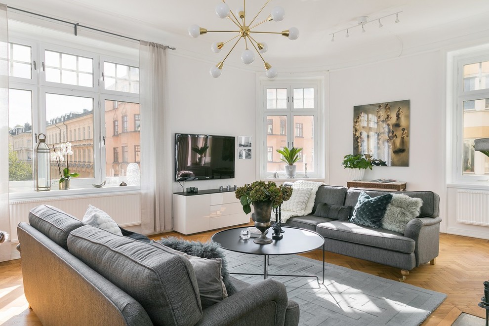 Scandinavian family room in Stockholm with white walls, medium hardwood floors and a wall-mounted tv.