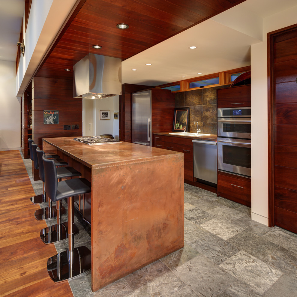 Inspiration for a modern galley open plan kitchen in Milwaukee with a farmhouse sink, flat-panel cabinets, dark wood cabinets, copper benchtops, stone tile splashback, stainless steel appliances, slate floors and with island.