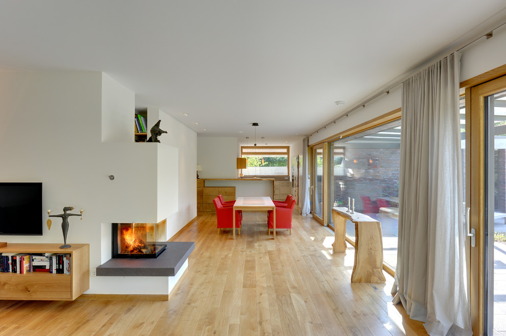 This is an example of a contemporary open plan dining in Berlin with white walls, light hardwood floors and a two-sided fireplace.