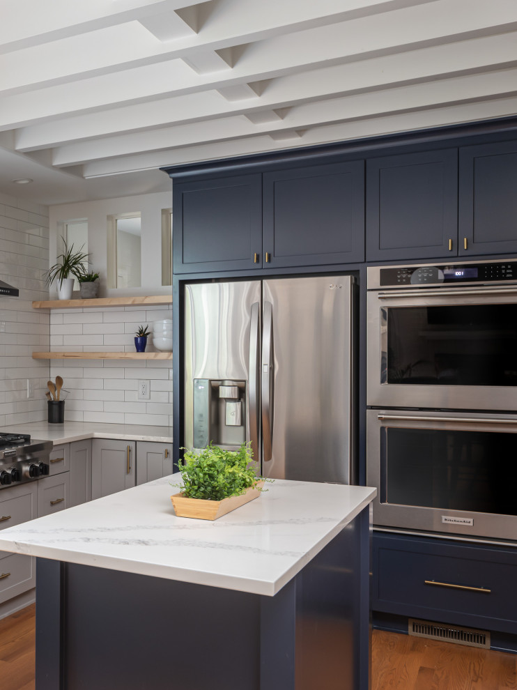 Open concept kitchen - mid-sized transitional u-shaped medium tone wood floor and brown floor open concept kitchen idea in Raleigh with an undermount sink, recessed-panel cabinets, blue cabinets, quartzite countertops, white backsplash, subway tile backsplash, stainless steel appliances, an island and white countertops
