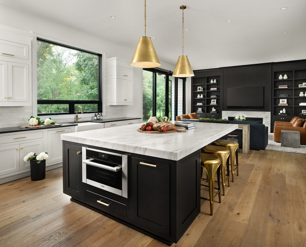 Photo of an expansive country u-shaped kitchen in Detroit with with island, a farmhouse sink, shaker cabinets, black cabinets, white splashback, stainless steel appliances, medium hardwood floors, brown floor and white benchtop.