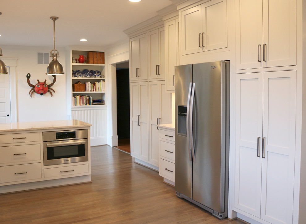 Large transitional galley medium tone wood floor and brown floor enclosed kitchen photo with a farmhouse sink, shaker cabinets, gray cabinets, quartzite countertops, stainless steel appliances, beige backsplash, subway tile backsplash and a peninsula