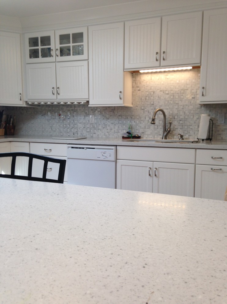 Eat-in kitchen - mid-sized coastal l-shaped eat-in kitchen idea with an undermount sink, beaded inset cabinets, white cabinets, solid surface countertops, gray backsplash, mosaic tile backsplash, white appliances and a peninsula