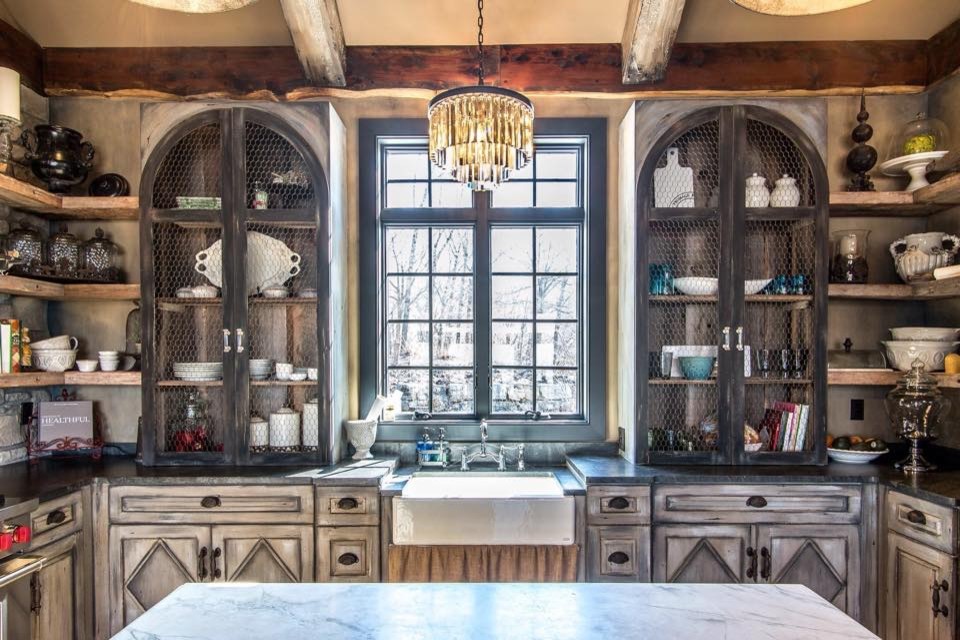 Example of a mid-sized mountain style l-shaped medium tone wood floor and brown floor eat-in kitchen design in St Louis with a farmhouse sink, distressed cabinets, gray backsplash, stainless steel appliances, an island and recessed-panel cabinets